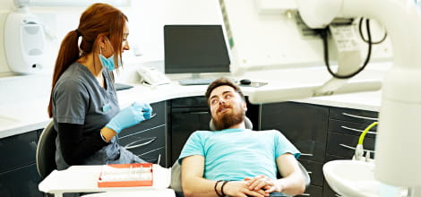 Female dental professional sitting next to a male patient in a dentist chair